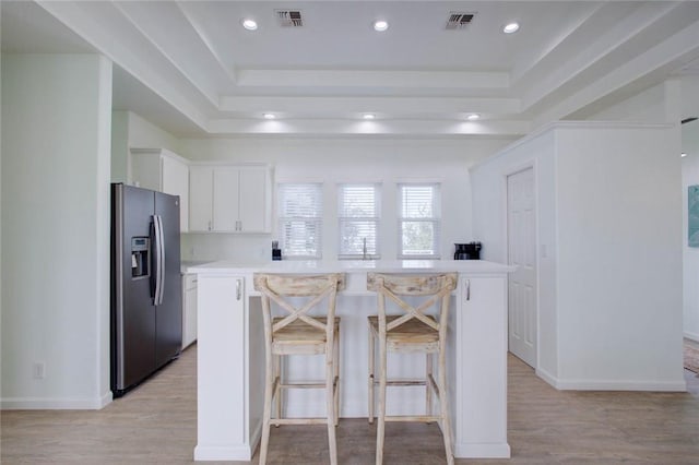 kitchen with white cabinets, stainless steel fridge with ice dispenser, a kitchen island, and a breakfast bar area