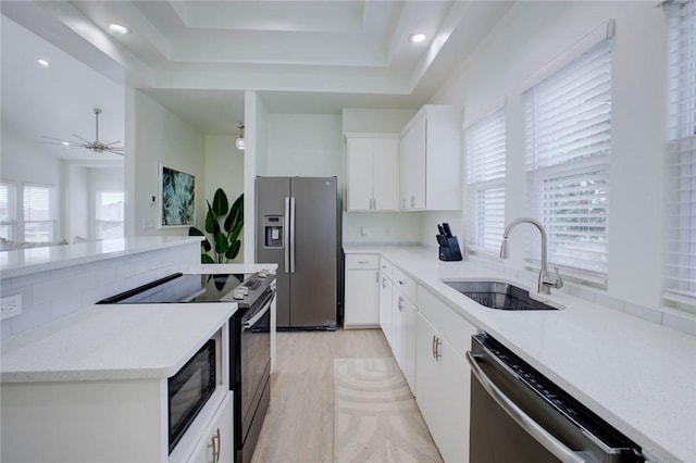 kitchen featuring stainless steel appliances, a tray ceiling, ceiling fan, sink, and white cabinets