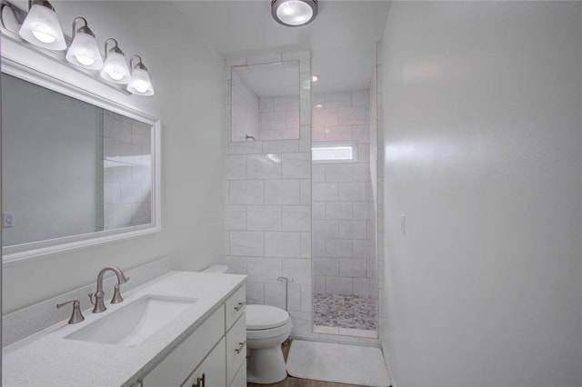 bathroom featuring a tile shower, vanity, and toilet