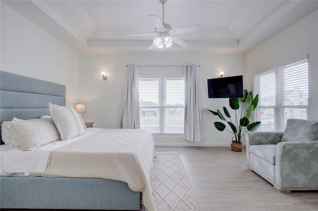 bedroom featuring ceiling fan, light wood-type flooring, and a tray ceiling