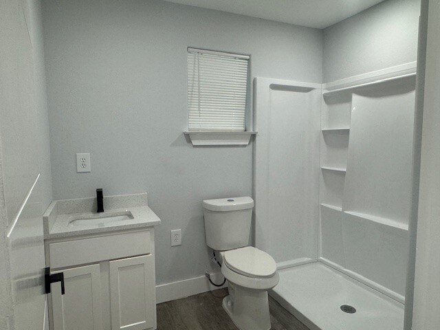 bathroom featuring a shower, wood-type flooring, vanity, and toilet