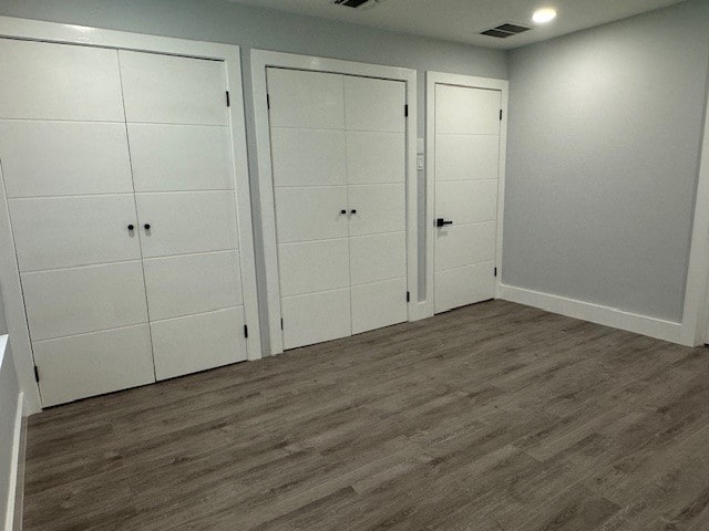 unfurnished bedroom with two closets and dark hardwood / wood-style floors