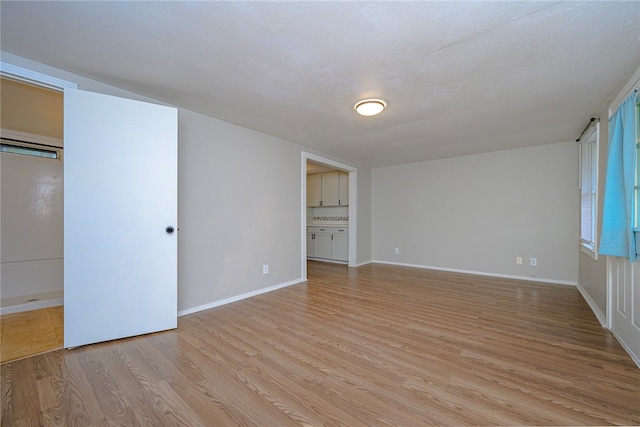 unfurnished bedroom with a textured ceiling, light wood finished floors, and baseboards