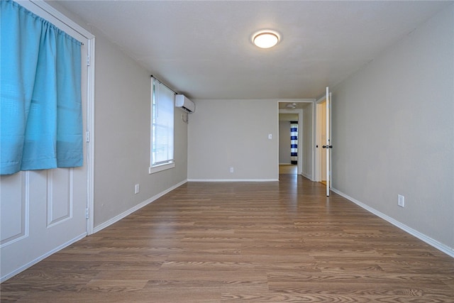 unfurnished room with a wall unit AC, wood finished floors, and baseboards