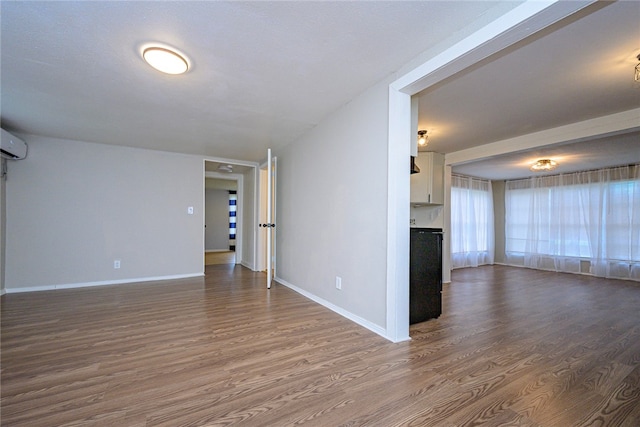 empty room with dark wood-style floors, a wall unit AC, and baseboards