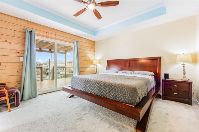 carpeted bedroom with ceiling fan, access to outside, wood walls, and a raised ceiling