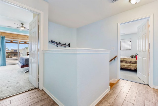 hall with baseboards, an upstairs landing, and wood finished floors