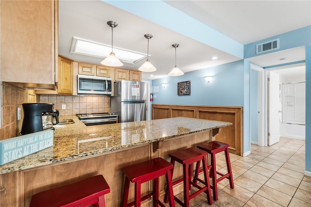 kitchen featuring stainless steel appliances, hanging light fixtures, decorative backsplash, a breakfast bar, and kitchen peninsula