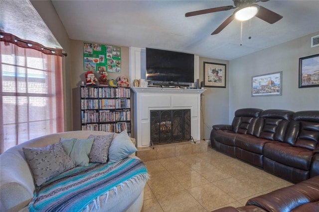 living room with ceiling fan, a tiled fireplace, and light tile patterned flooring