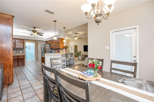 dining area with light tile patterned floors, arched walkways, visible vents, and ceiling fan with notable chandelier