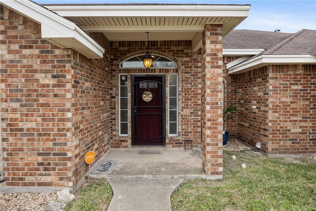 view of exterior entry with brick siding and roof with shingles