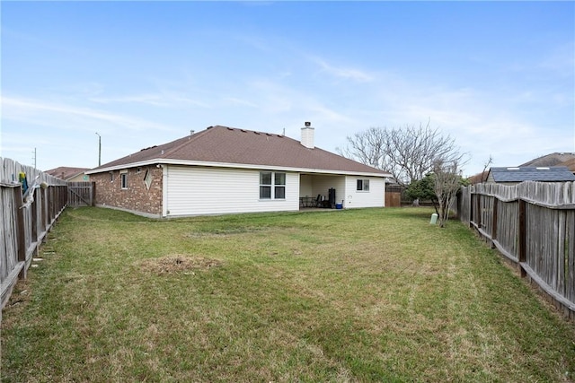 rear view of house with a fenced backyard, a chimney, a lawn, and brick siding