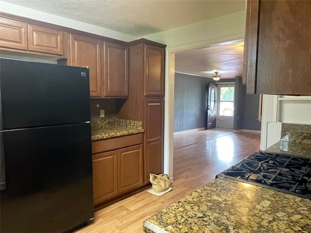 kitchen with stone countertops, black refrigerator, a textured ceiling, and light hardwood / wood-style flooring