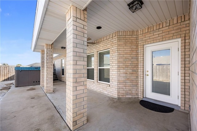 property entrance featuring brick siding, a patio area, fence, and a hot tub