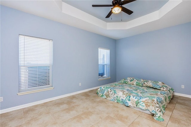 bedroom featuring light tile patterned floors, a tray ceiling, a ceiling fan, and baseboards