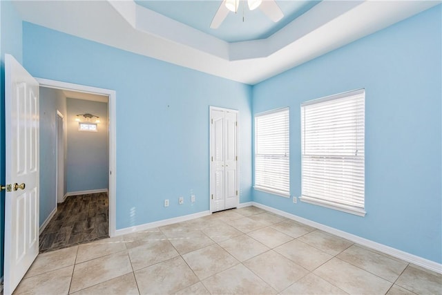 unfurnished bedroom featuring light tile patterned floors, baseboards, a tray ceiling, and ceiling fan