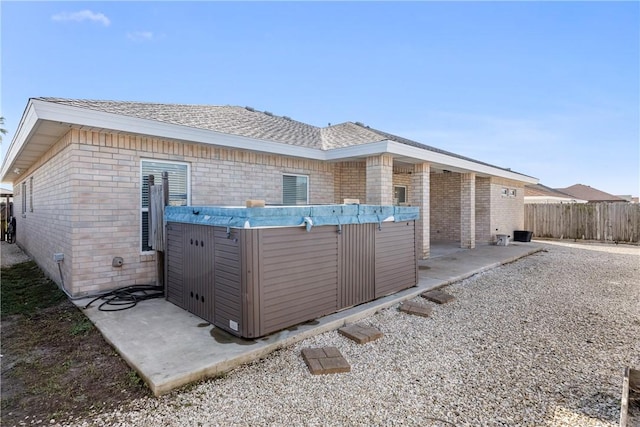 view of side of property with brick siding, roof with shingles, a patio area, and fence