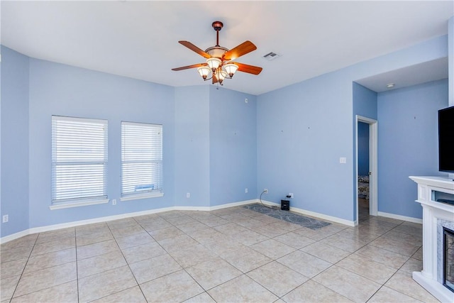 spare room with light tile patterned floors, ceiling fan, a fireplace, and baseboards