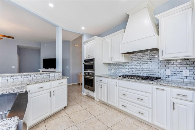 kitchen featuring light tile patterned floors, tasteful backsplash, white cabinets, custom range hood, and stainless steel appliances