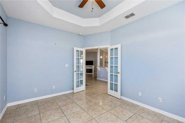 empty room with baseboards, visible vents, a ceiling fan, a tray ceiling, and french doors