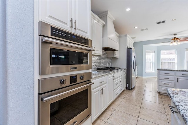 kitchen with light stone counters, custom exhaust hood, stainless steel appliances, visible vents, and white cabinets