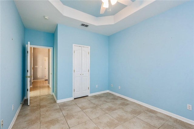 unfurnished bedroom with light tile patterned floors, visible vents, baseboards, a closet, and a tray ceiling