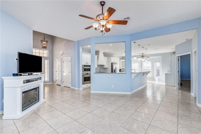 living area with light tile patterned floors, a high end fireplace, a ceiling fan, and baseboards