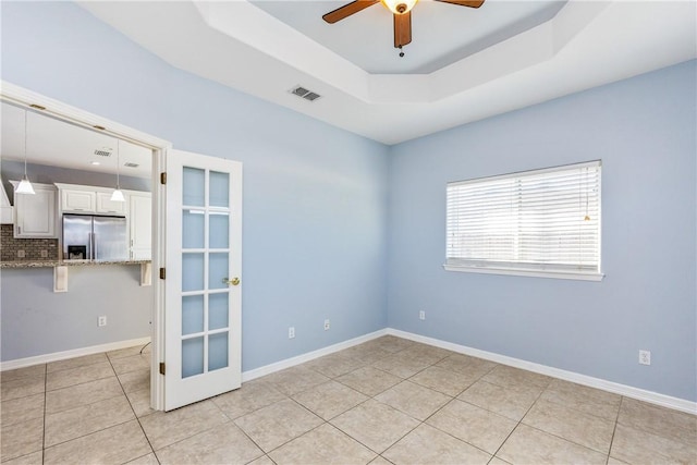 empty room with baseboards, visible vents, ceiling fan, a tray ceiling, and light tile patterned flooring