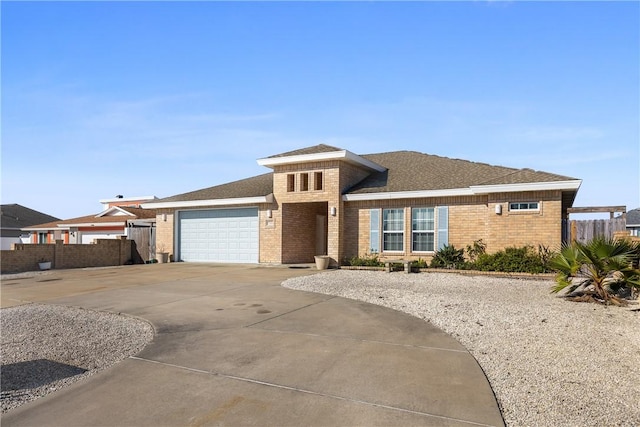 prairie-style home with a garage, brick siding, driveway, and fence