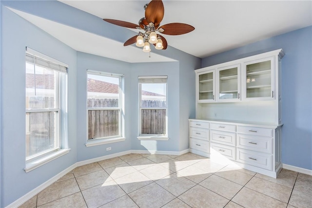 unfurnished dining area featuring ceiling fan, light tile patterned flooring, and baseboards