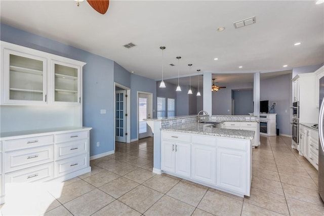 kitchen with glass insert cabinets, decorative light fixtures, a kitchen island with sink, white cabinetry, and a sink