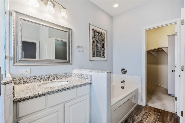 full bath with vanity, baseboards, a spacious closet, a bath, and wood tiled floor