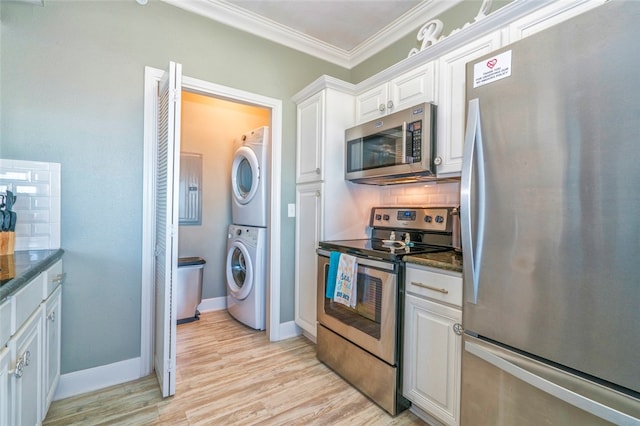 kitchen with stainless steel appliances, stacked washing maching and dryer, white cabinetry, dark stone countertops, and crown molding