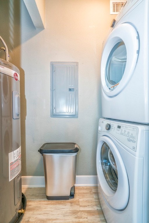 laundry area with electric panel, stacked washer and clothes dryer, light hardwood / wood-style flooring, and electric water heater