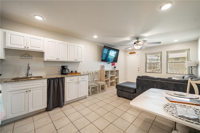 kitchen with a sink, light stone counters, ceiling fan, light tile patterned floors, and white cabinets