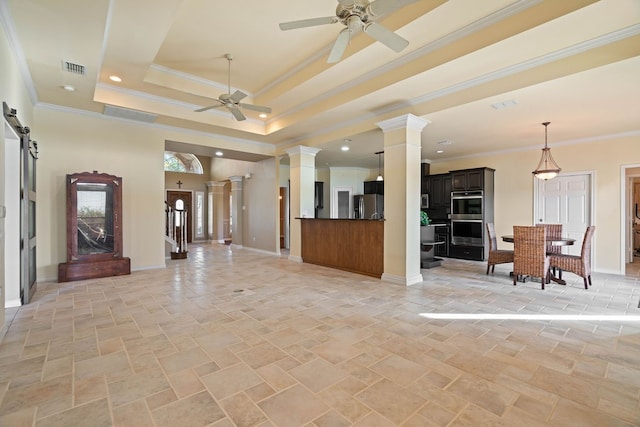 living room with ceiling fan, decorative columns, a tray ceiling, ornamental molding, and a barn door