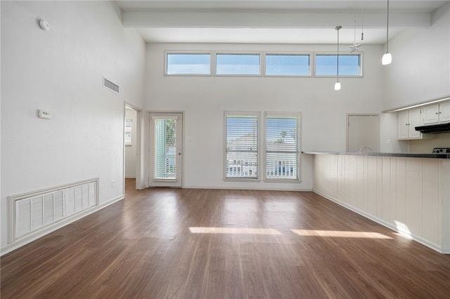 unfurnished living room with a wealth of natural light, beamed ceiling, a towering ceiling, and dark hardwood / wood-style flooring