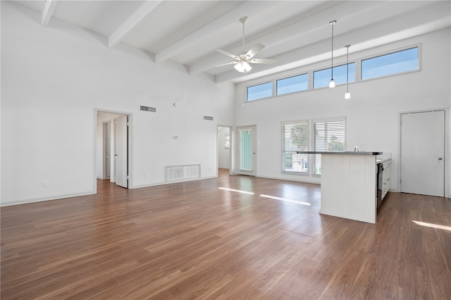 unfurnished living room featuring dark hardwood / wood-style flooring, beamed ceiling, ceiling fan, and a towering ceiling