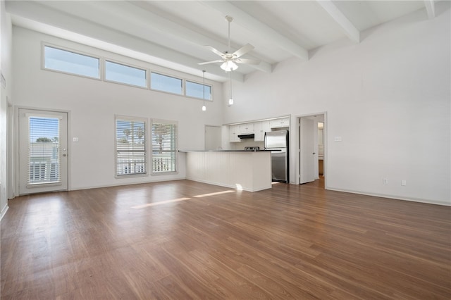 unfurnished living room featuring dark wood-type flooring, ceiling fan, a high ceiling, and beam ceiling