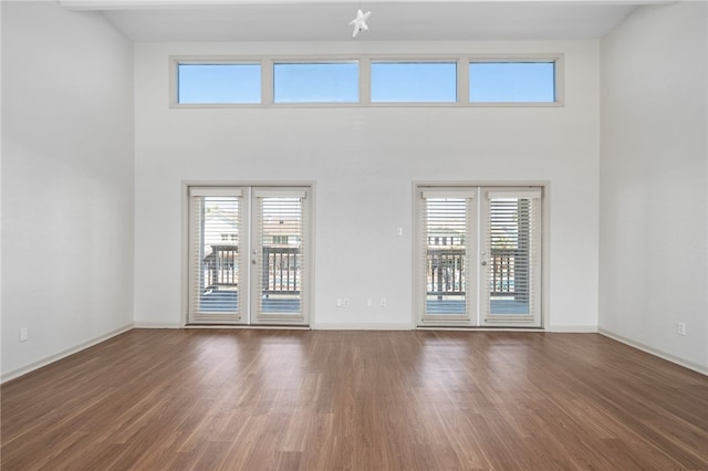 empty room featuring dark wood-type flooring, a wealth of natural light, a towering ceiling, and french doors