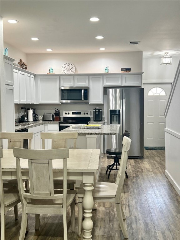 kitchen featuring a kitchen bar, wood-type flooring, light stone counters, a center island, and appliances with stainless steel finishes