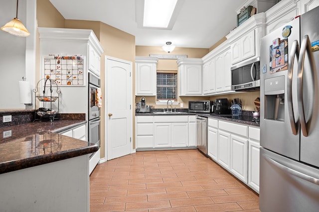 kitchen with white cabinets, sink, appliances with stainless steel finishes, decorative light fixtures, and dark stone countertops