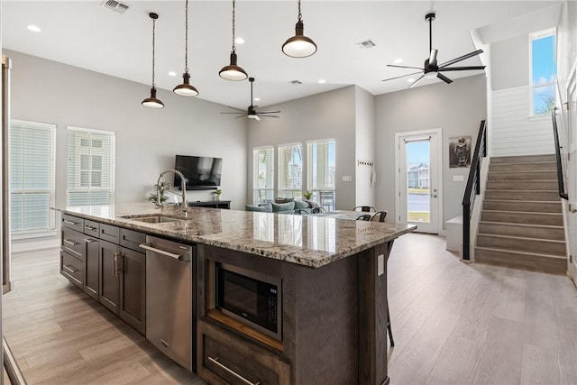 kitchen featuring open floor plan, a ceiling fan, light wood finished floors, dishwasher, and a sink