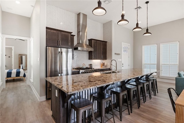 kitchen featuring visible vents, a high ceiling, wall chimney exhaust hood, a sink, and freestanding refrigerator