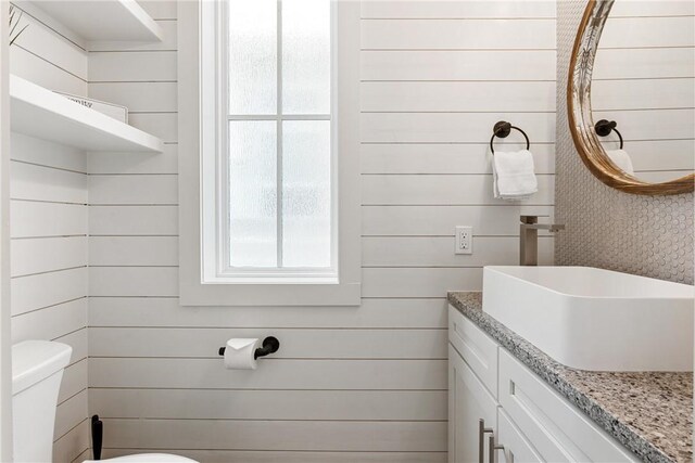 bathroom with wood walls, vanity, and toilet