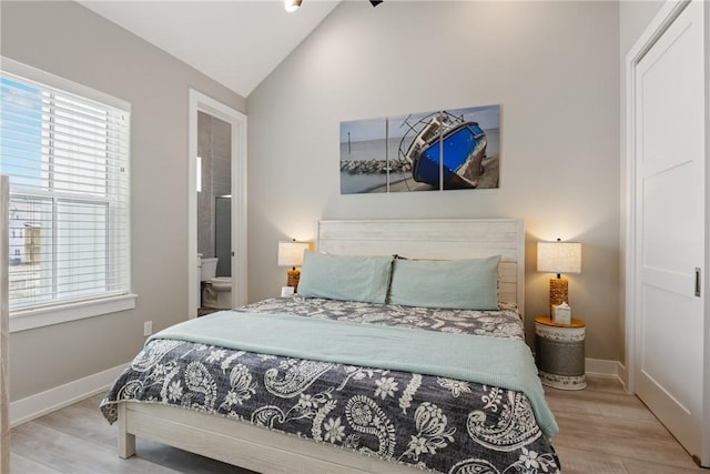 bedroom featuring baseboards, wood finished floors, ensuite bath, and vaulted ceiling