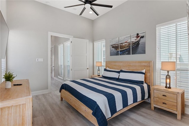 bedroom with baseboards, a high ceiling, a ceiling fan, recessed lighting, and wood finished floors