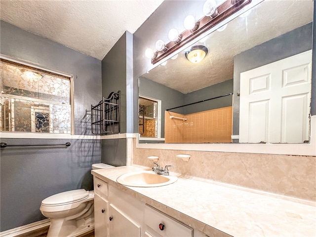 bathroom featuring toilet, vanity, a textured ceiling, and a tile shower