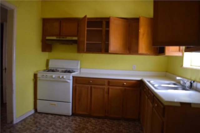 kitchen featuring brown cabinets, under cabinet range hood, a sink, light countertops, and white gas range