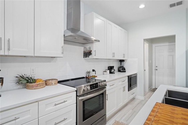 kitchen with built in microwave, wall chimney exhaust hood, tasteful backsplash, stainless steel range with electric cooktop, and white cabinets